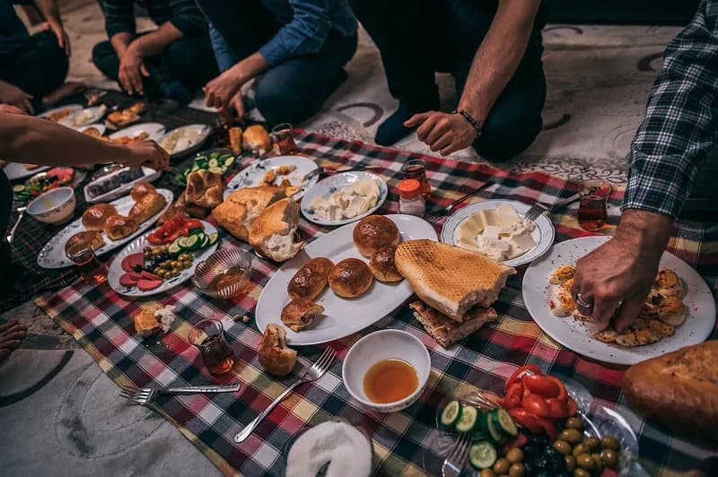 Hidangan sahur bersama di atas taplak kotak-kotak: roti, keju, telur, sayur, buah zaitun, dan teh