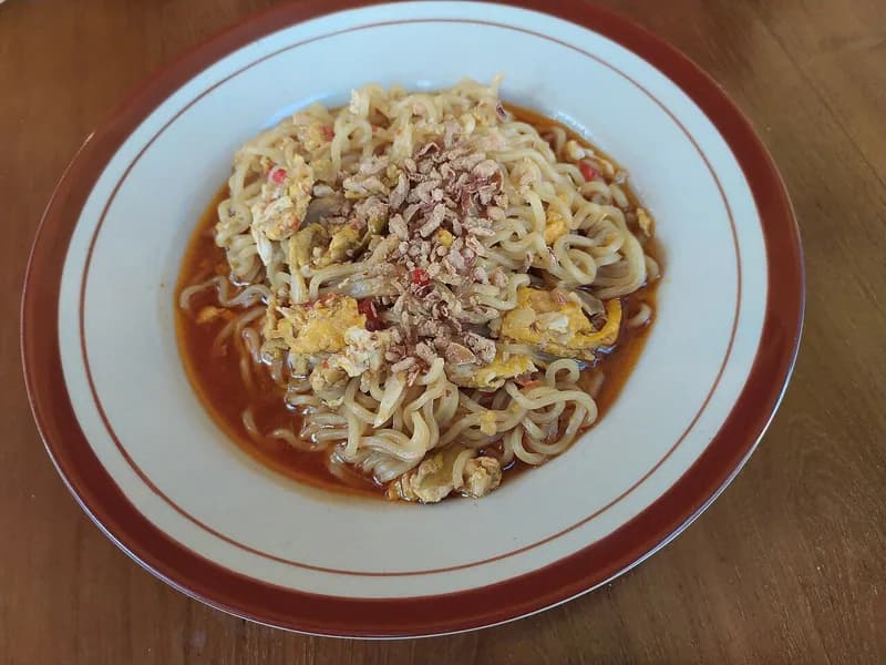 Sepiring mie nyemek berkuah merah kental dengan orak-arik telur dan bawang goreng
