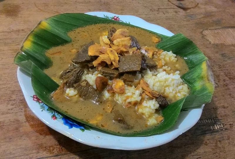 Sepiring nasi gandul khas Pati beralas daun pisang dengan kuah cokelat, irisan daging sapi, dan bawang goreng