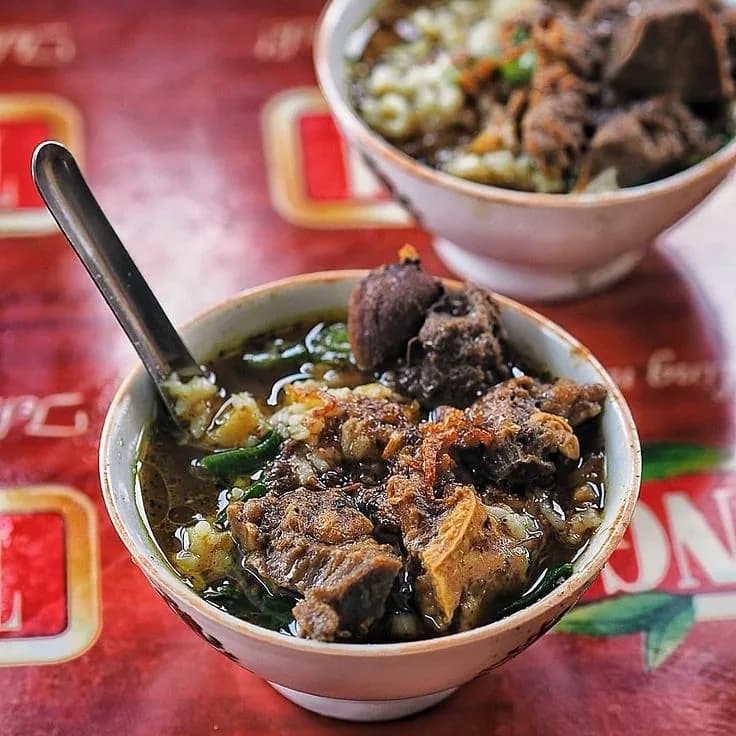 Semangkuk nasi grombyang Pemalang berkuah cokelat gelap dengan potongan daging kerbau dan bawang goreng