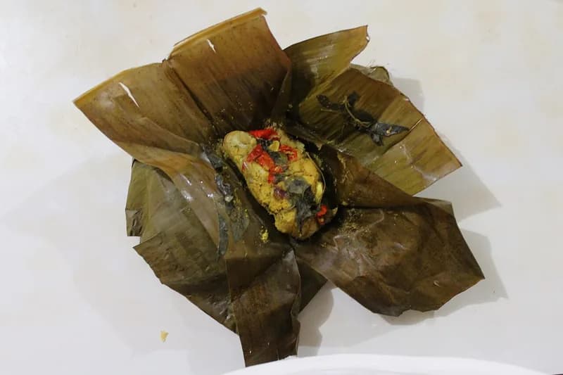 Pepes tahu matang dengan irisan cabai merah dan daun kemangi dalam bungkus daun pisang terbuka