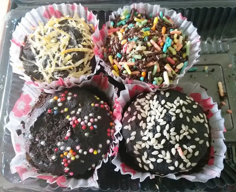 Empat brownies kukus cokelat dalam cup kertas dengan topping keju, meses warna-warni, dan wijen