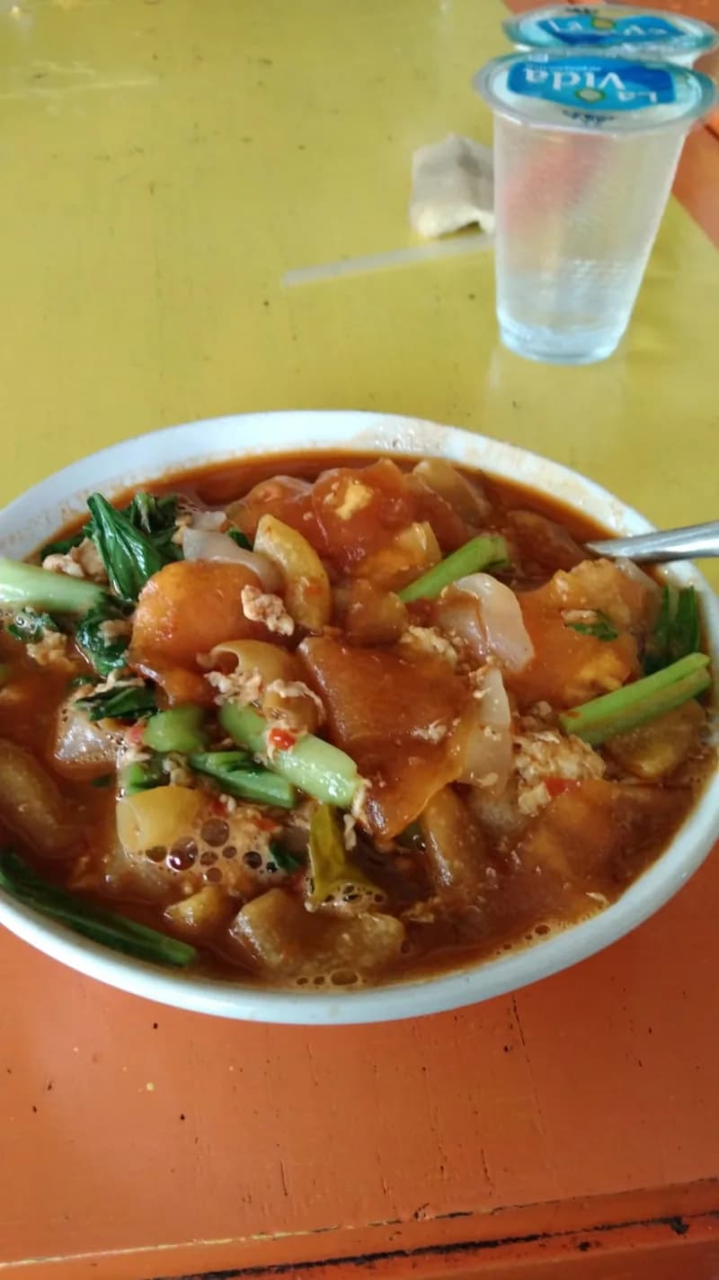Semangkuk seblak kuah merah pedas berisi kerupuk basah, orak-arik telur, dan sawi hijau