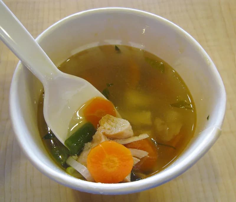 Semangkuk sop ayam berkuah bening dengan potongan ayam, irisan wortel, dan buncis