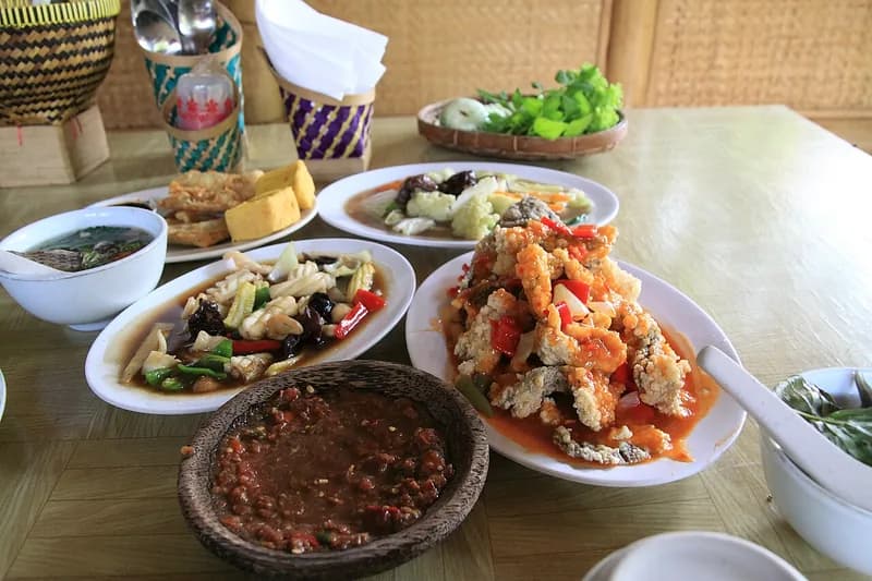 Meja makan rumah makan Sunda berisi sambal, tahu tempe goreng, tumis sayur, lauk asam manis, dan lalapan