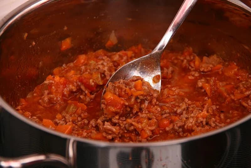 Saus bolognese daging cincang dengan potongan wortel dan tomat di dalam panci stainless