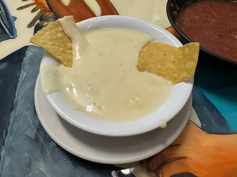 Semangkuk saus keju putih yang kental dan creamy dengan dua keripik tortila tercelup di dalamnya