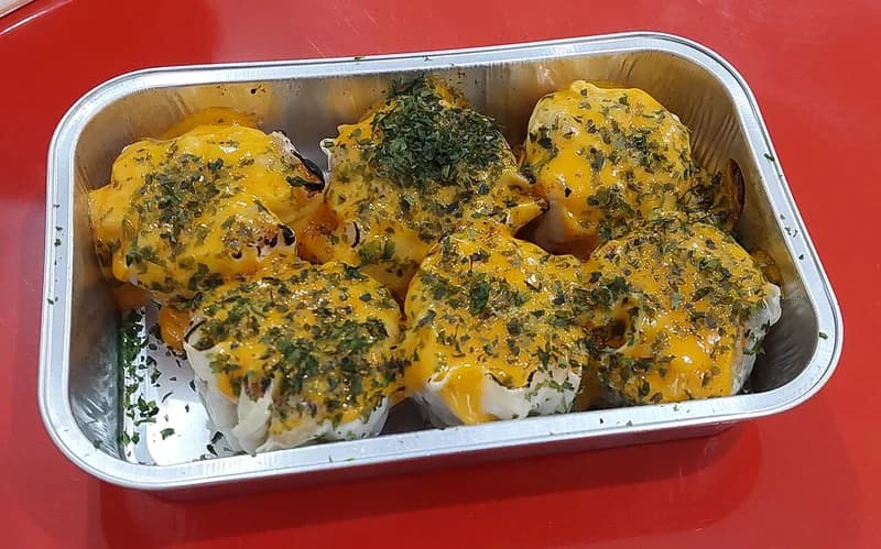Dimsum mentai berlapis saus mentai oranye keemasan bertabur daun parsley kering di wadah aluminium