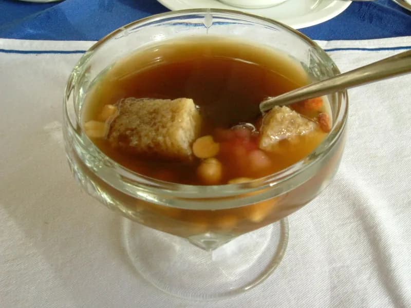 Sekoteng jahe hangat dalam gelas kaki kaca berisi potongan roti, kacang tanah, dan isian merah muda
