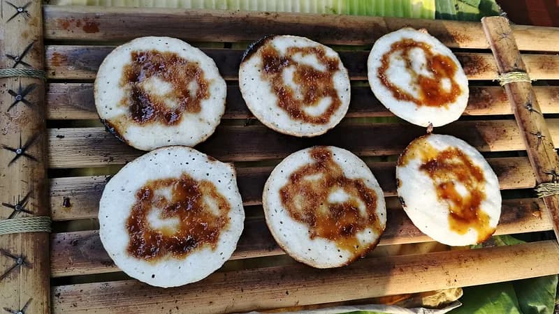 Enam serabi putih dengan siraman gula merah cair tertata di atas anyaman bambu