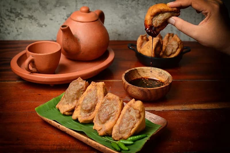 Tahu bakso goreng di atas daun pisang dengan cabai rawit dan mangkuk kecil saus kecap pedas