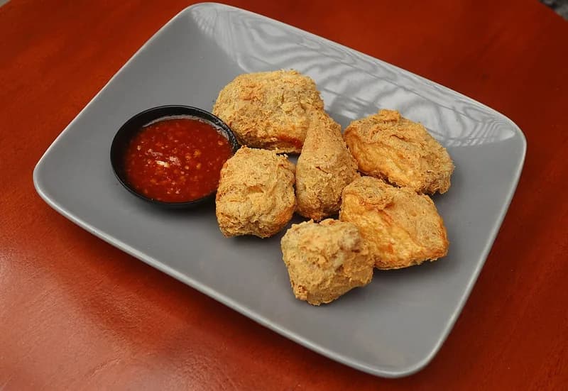 Tujuh potong tahu walik goreng renyah di piring abu-abu dengan semangkuk kecil saus sambal