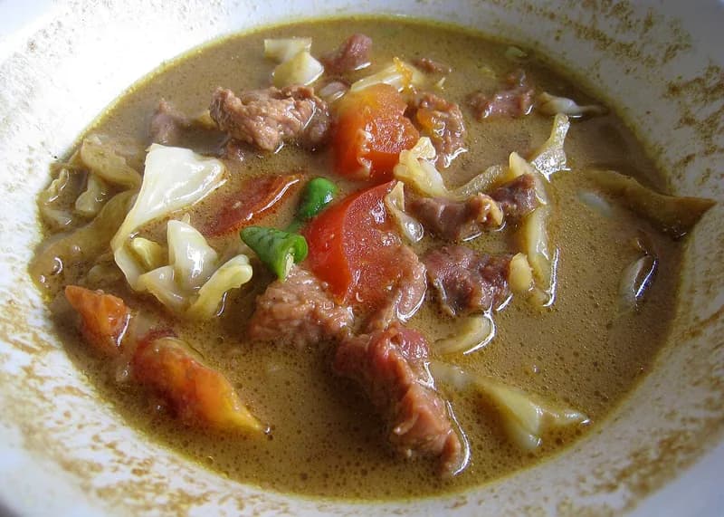 Tongseng kambing berkuah santan kecokelatan dengan potongan daging, kol, tomat, dan cabai hijau
