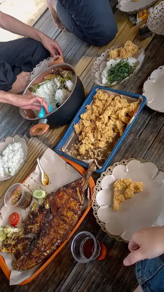 Beberapa orang makan bersama secara lesehan dengan nasi, ikan bakar, dan sayuran