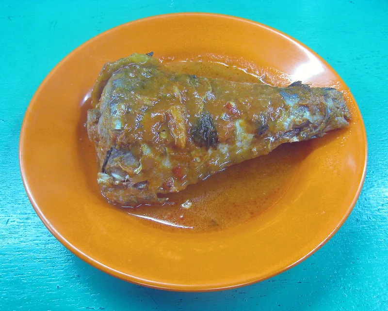 Potongan ikan asam padeh ala Padang berlumur kuah jingga di piring oranye