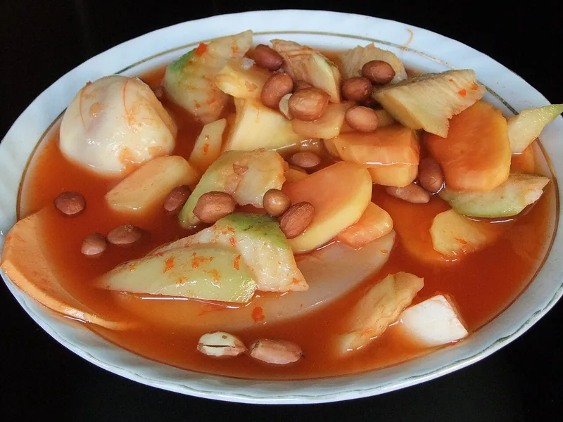 Semangkuk asinan Bogor berisi potongan buah mengkal dan kacang tanah dalam kuah cabai merah