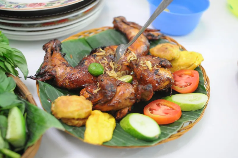 Ayam panggang berbumbu kecap di atas daun pisang dengan tomat, mentimun, tempe goreng, dan lalapan kemangi