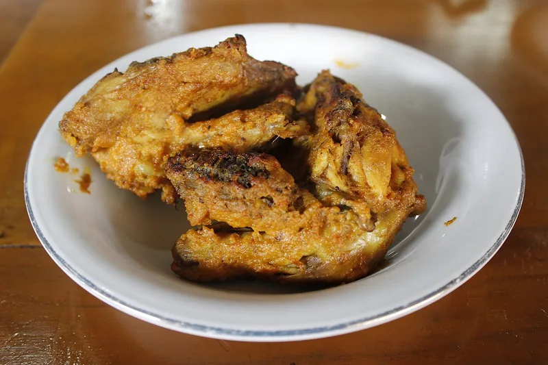 Potongan ayam bakar berbumbu kuning kecokelatan di piring putih