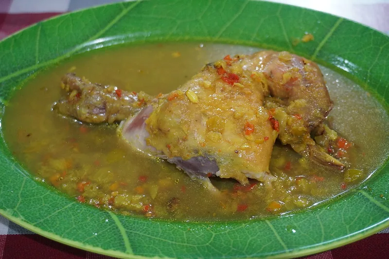 Potongan ayam betutu Gilimanuk terendam kuah bumbu base genep kekuningan dengan irisan cabai
