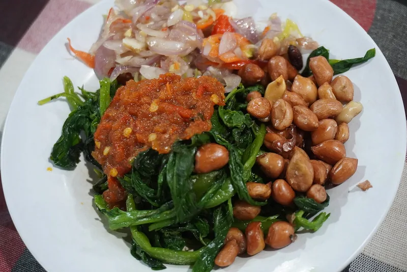 Pelengkap ayam betutu berupa kangkung rebus, kacang tanah goreng, sambal merah, dan sambal matah