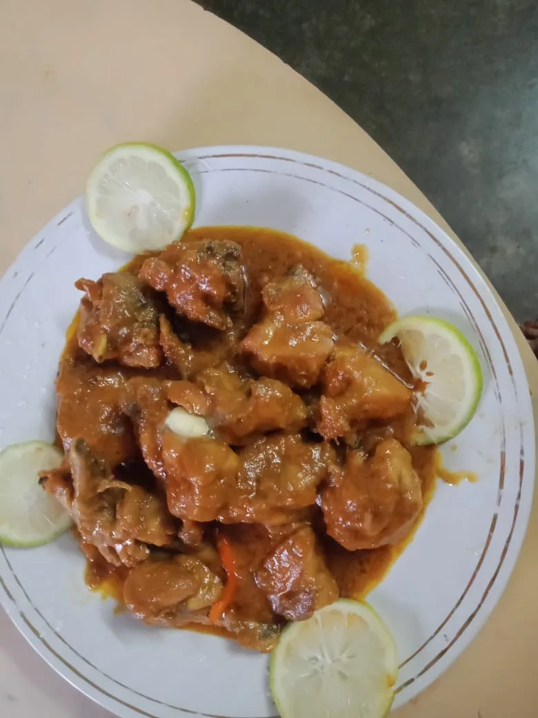 Potongan ayam goreng dalam saus mentega kental kecokelatan dengan irisan jeruk nipis di pinggir piring