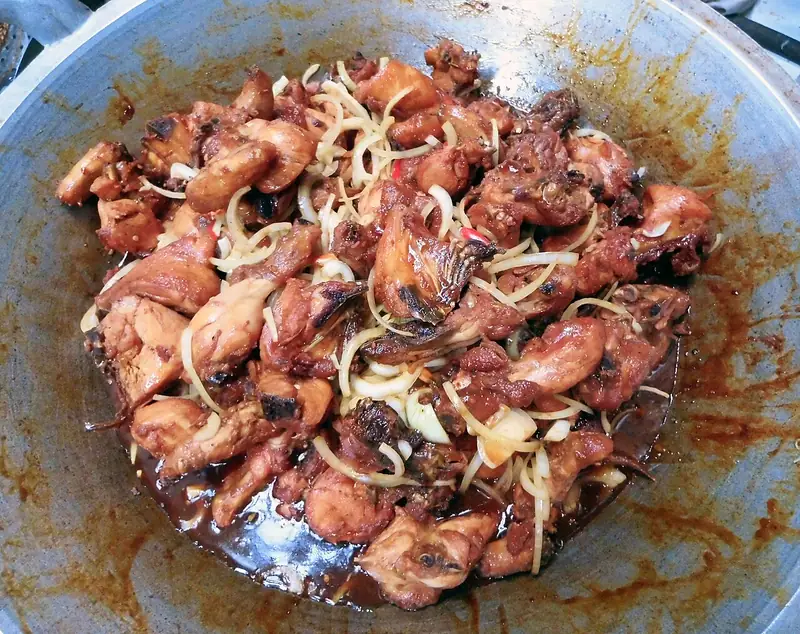 Ayam kecap berwarna cokelat mengilap dengan irisan bawang bombai di dalam wajan