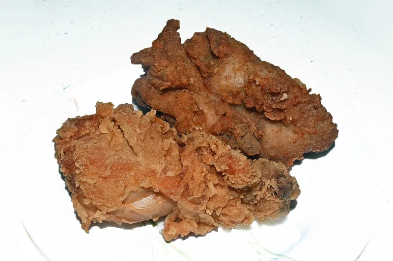 Dua potong ayam goreng berbalut tepung renyah keemasan di piring putih
