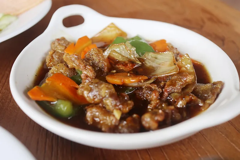 Sapi lada hitam dengan wortel, paprika hijau, dan kol dalam saus cokelat di pinggan putih