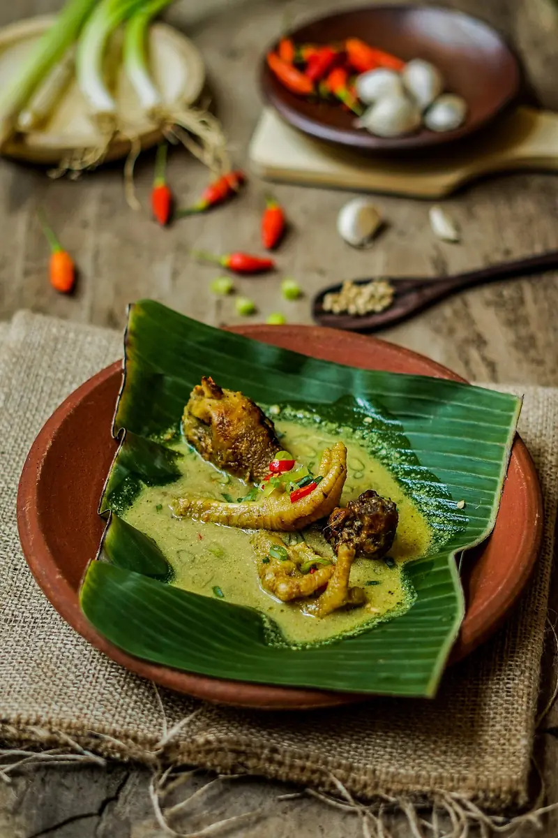 Ayam lodho khas Tulungagung beralas daun pisang di piring tanah liat dengan cabai rawit