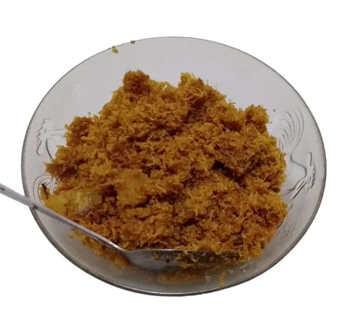 Semangkuk serundeng ayam cokelat dengan potongan ayam di dalamnya dan sendok