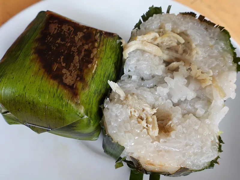 Lemper ketan terbelah memperlihatkan isian ayam suwir di samping lemper utuh berbungkus daun pisang