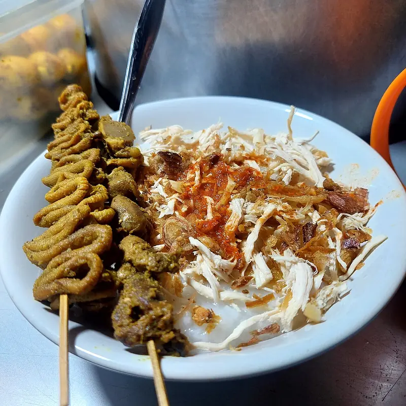 Bubur ayam bertabur ayam suwir, bawang goreng, dan sambal, disajikan dengan sate usus dan sate ampela