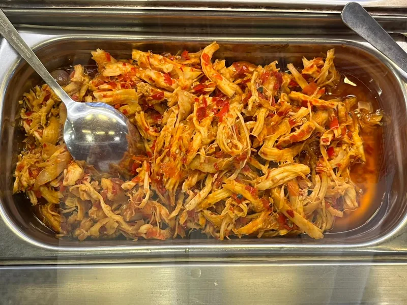 Ayam suwir berbumbu cabai merah dengan minyak kemerahan di wadah stainless prasmanan dan sendok sayur