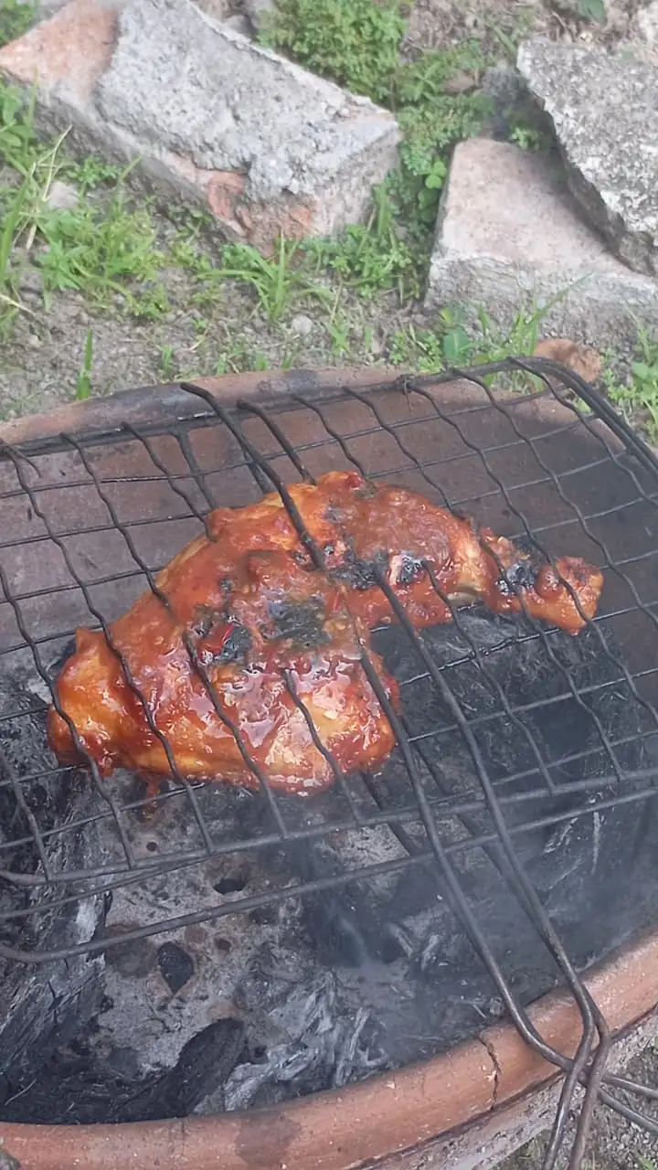 Ayam berlumur bumbu cabai merah dibakar dalam jepitan kawat di atas bara arang