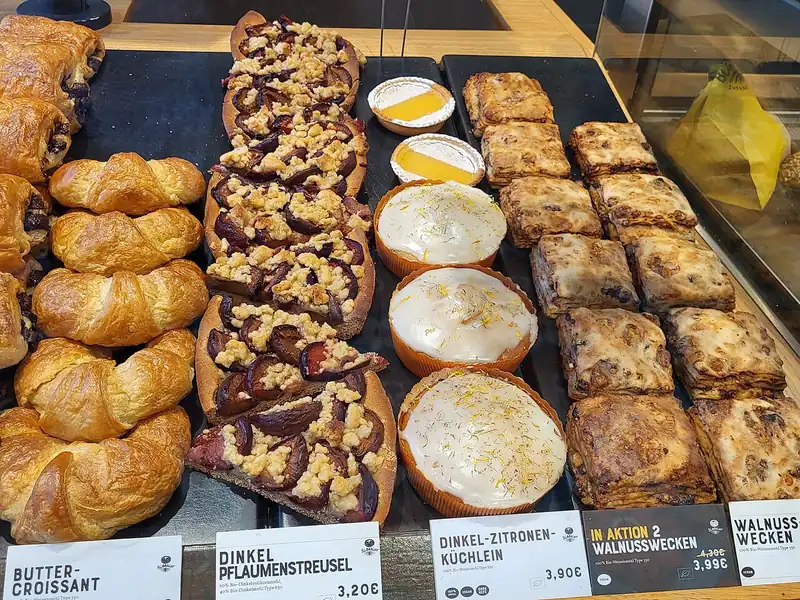 Etalase bakery berisi croissant mentega, kue streusel plum, tart lemon, dan roti kenari