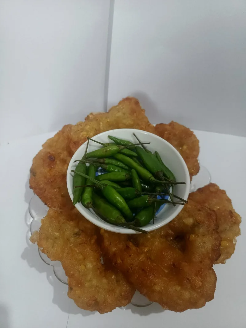 Bakwan jagung goreng tersusun melingkar mengelilingi mangkuk kecil berisi cabai rawit hijau