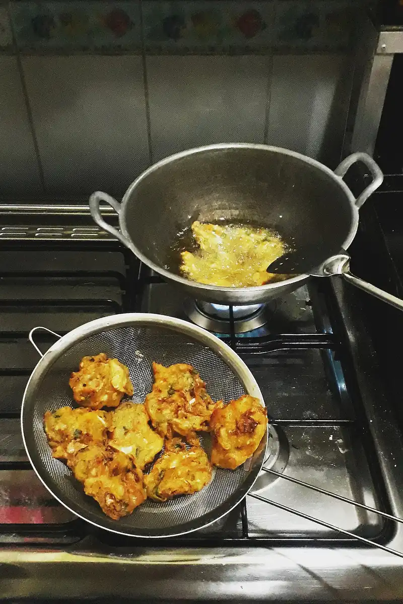 Bakwan goreng kecokelatan ditiriskan di saringan di samping wajan