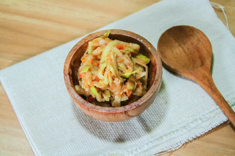 Sambal mangga muda serut dengan cabai dalam mangkuk kayu kecil di atas serbet