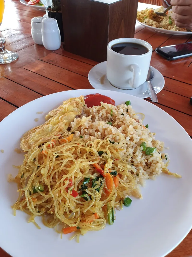 Bihun goreng berwarna terang dengan wortel dan daun bawang di samping nasi goreng dan telur dadar
