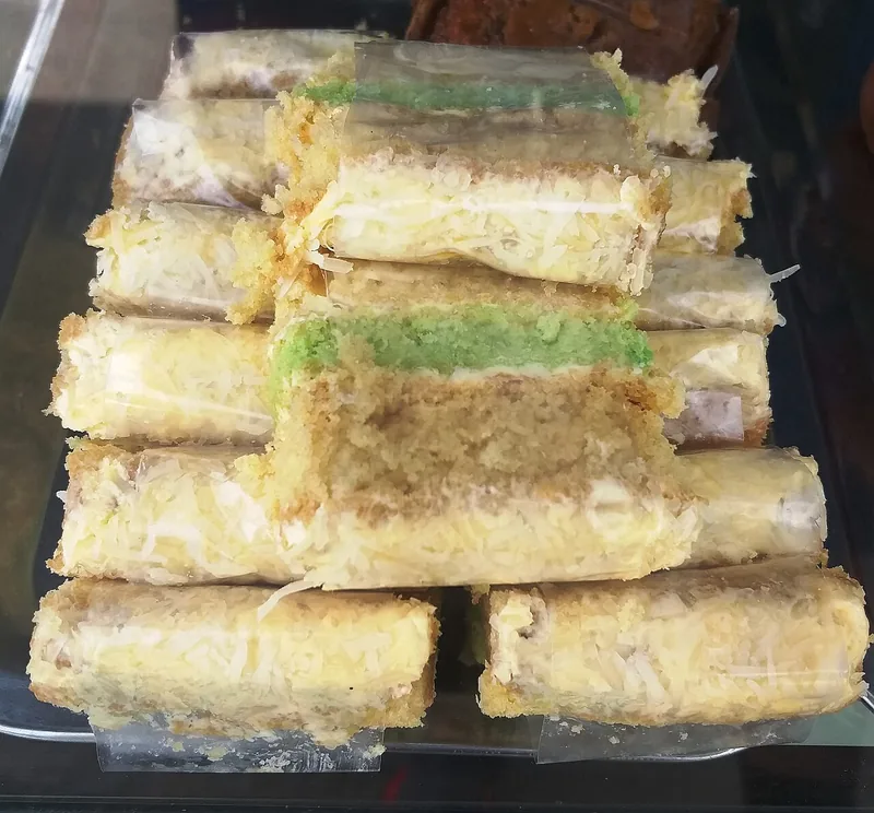 Potongan bolu kukus keju berlapis hijau pandan dengan taburan keju parut dibungkus plastik