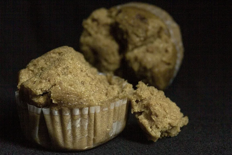 Bolu kukus cokelat muda dalam cup kertas dengan bagian atas merekah dan potongan yang dipatahkan