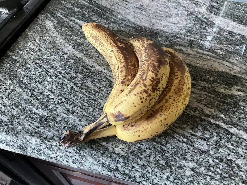 Tiga buah pisang sangat matang dengan kulit kuning penuh bintik cokelat di meja granit