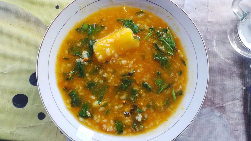 Bubur Manado dengan daun sayuran hijau segar dan potongan singkong dalam mangkuk putih