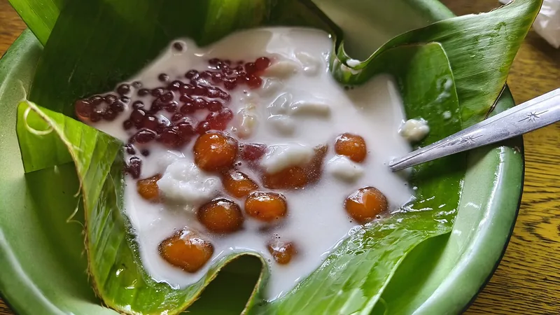Bubur sumsum disajikan bersama bubur candil, mutiara merah, dan kuah santan di piring daun pisang
