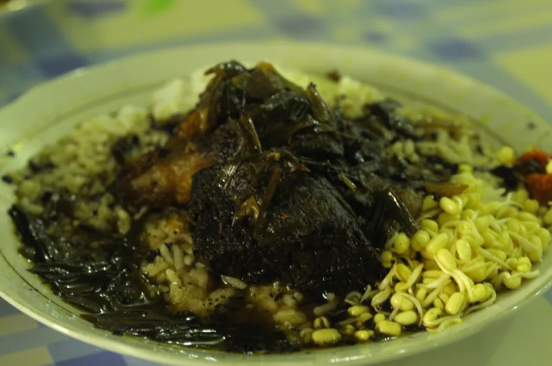 Nasi dengan kuah rawon gelap, daging, dan tauge pendek dalam satu piring