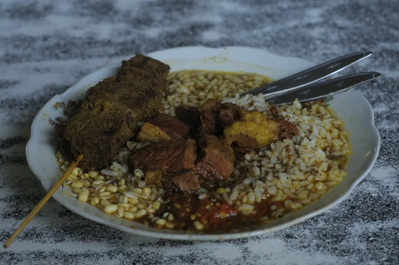 Nasi rawon dengan potongan daging, tauge, dan lauk tambahan di piring putih
