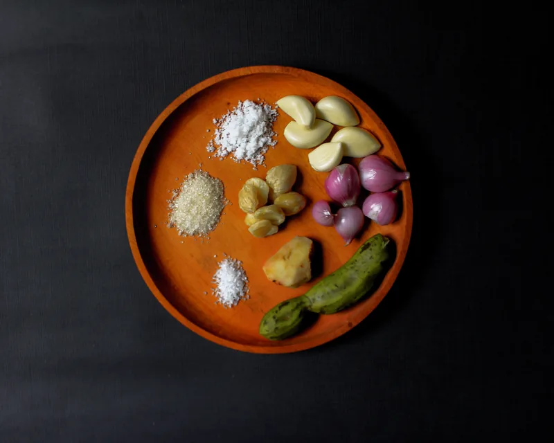 Bumbu sayur asem di piring kayu: bawang putih, bawang merah, kemiri, lengkuas, asam jawa, gula, dan garam