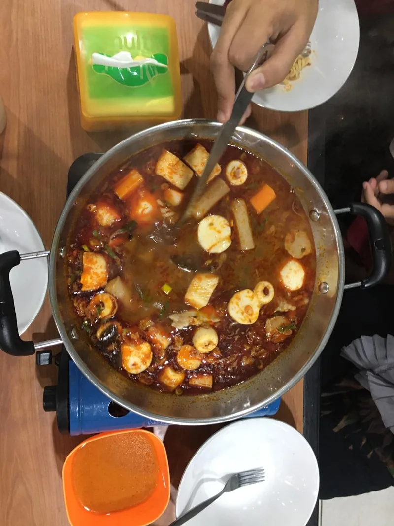 Panci seblak berkuah merah pedas berisi bakso, sosis, tahu, dan kerupuk di atas kompor portabel