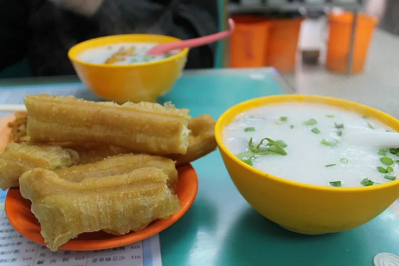 Potongan cakwe di piring oranye disajikan bersama mangkuk bubur nasi bertabur daun bawang