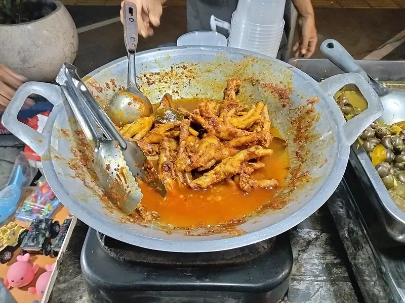 Ceker ayam dimasak dalam wajan dengan kuah bumbu cabai merah berminyak di kompor pedagang